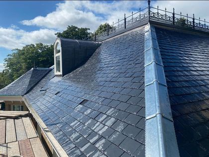 Slate roof with dormer and decorative ridge trim under a clear sky