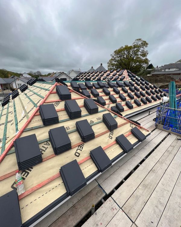 Roof under construction with rows of dark tiles, insulation, and scaffolding under a cloudy sky