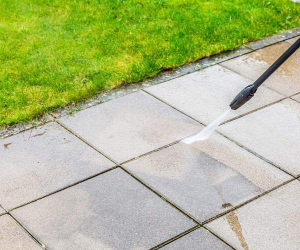 Pressure washing concrete patio beside a green lawn