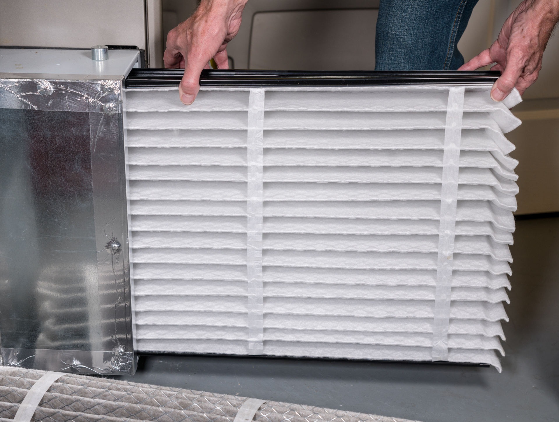 Person replacing HVAC air filter, white accordion-style filter with black frame, indoors.