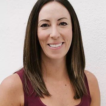 Woman with dark hair smiling, wearing a burgundy tank top, standing against a white background.