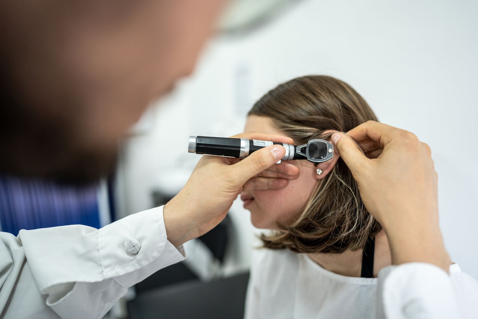 Doctor examining a patient's ear with an otoscope in a clinical setting.