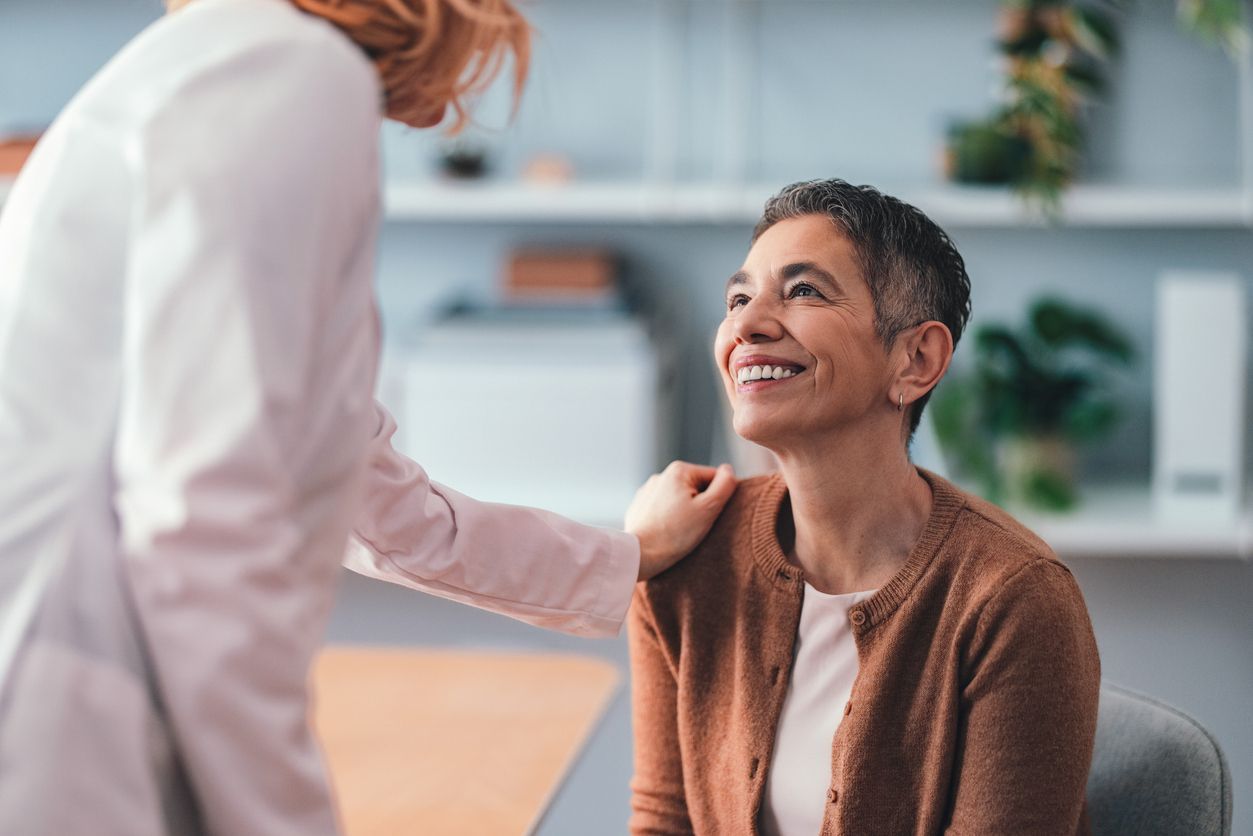 Doctor with hand on patient's shoulder, smiling warmly, in a well-lit office.