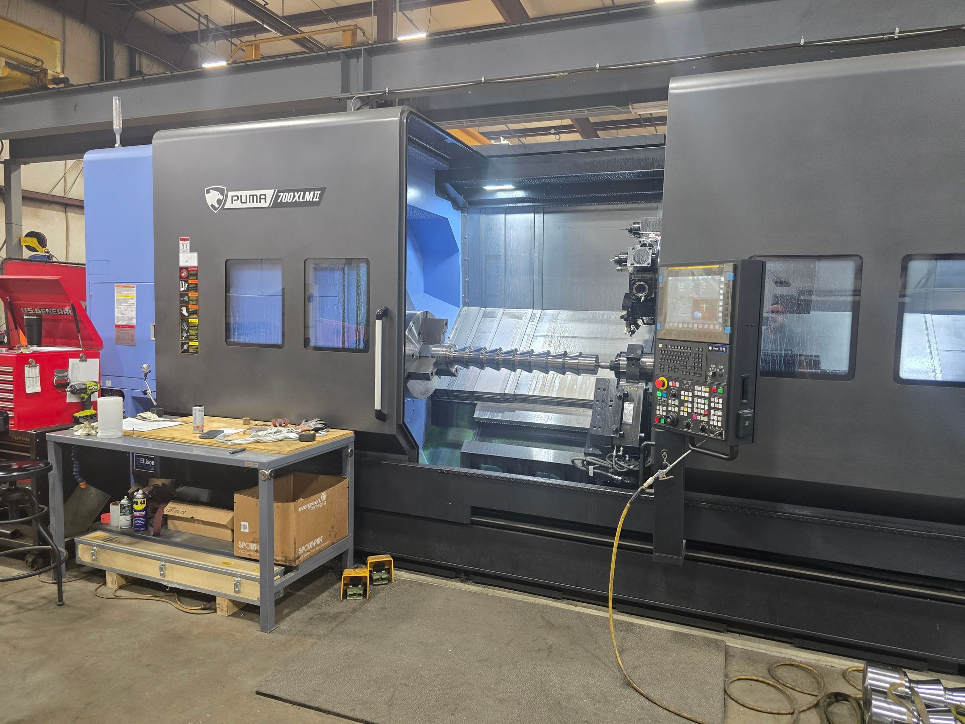 Large industrial CNC machine in a workshop, with a worktable and tools in front.