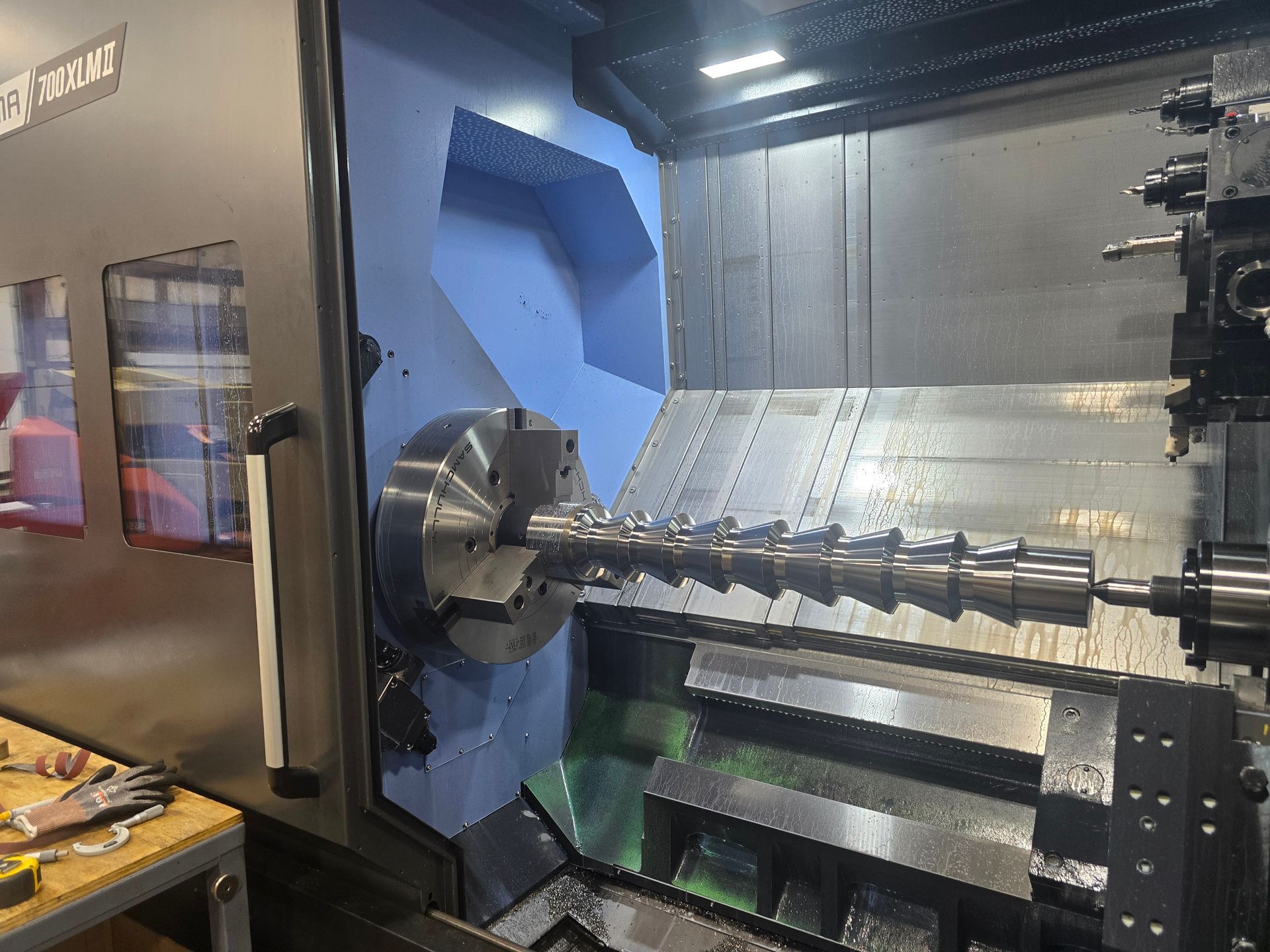 CNC lathe machining a metal shaft inside a factory, with blue interior panels and metal chips below