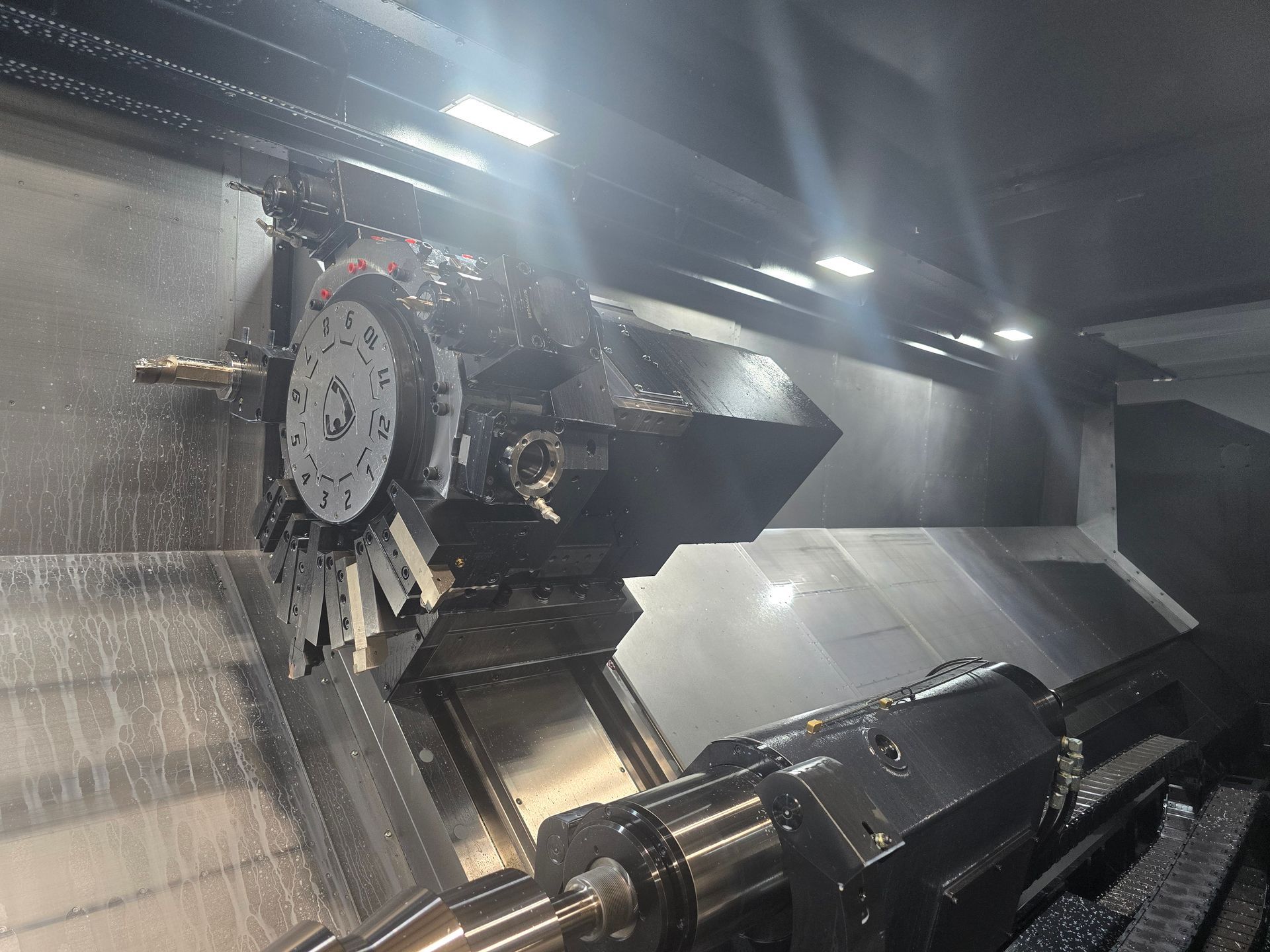 Interior of a CNC machine with metal workpiece and spindle under bright overhead lights
