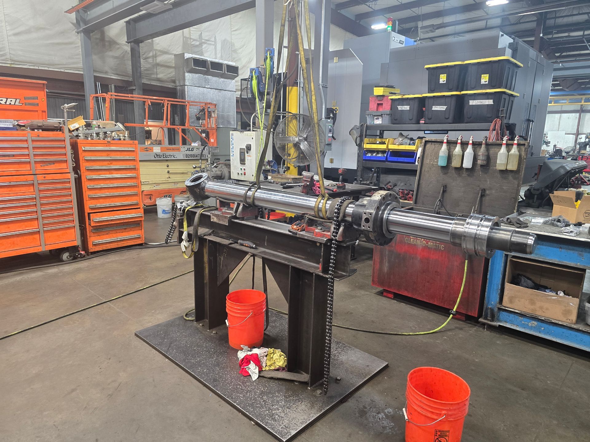 Industrial machine on factory floor with orange tool carts and buckets nearby