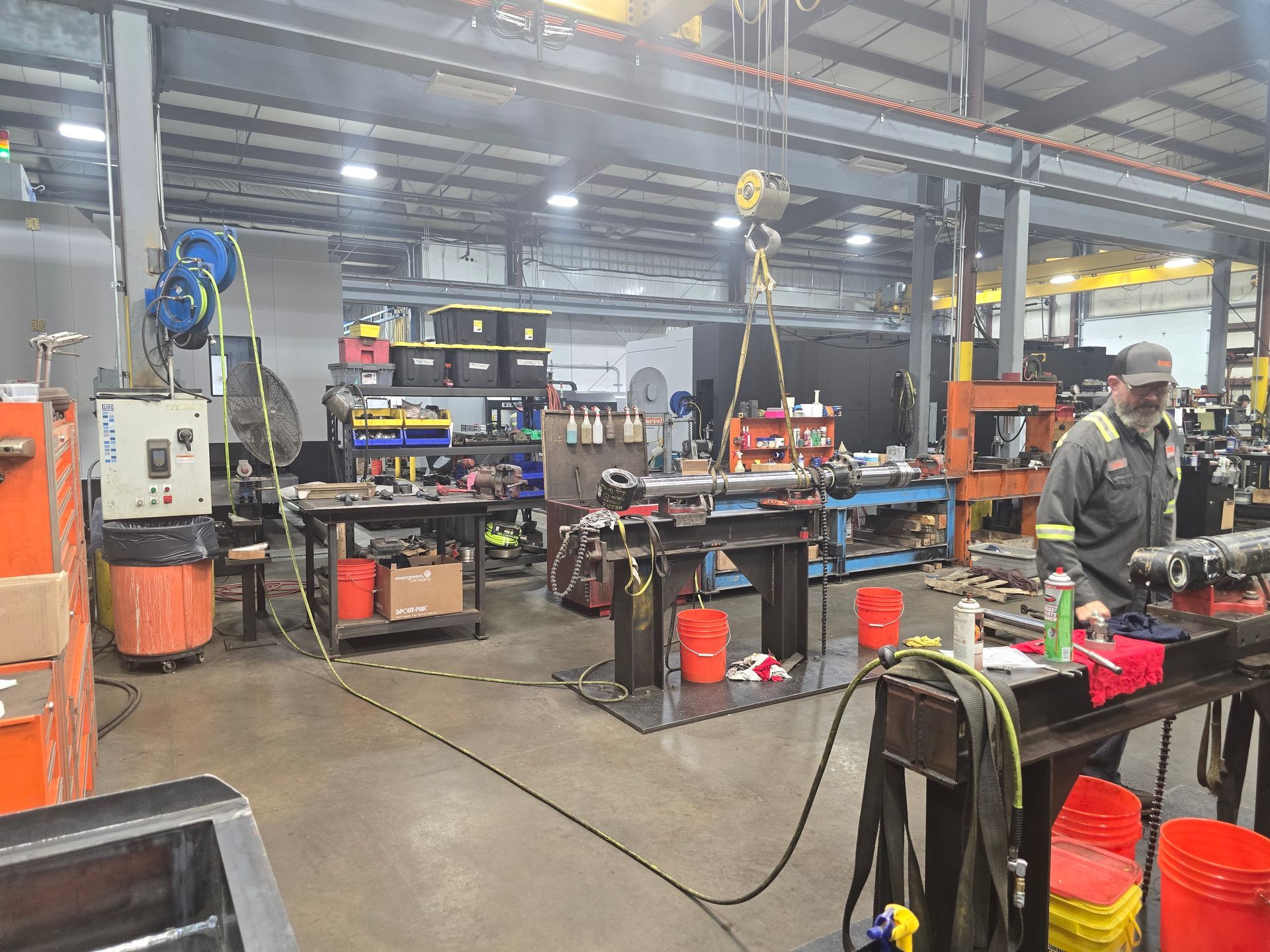Industrial workshop with machinery, workbenches, tools, and red buckets under bright overhead lights