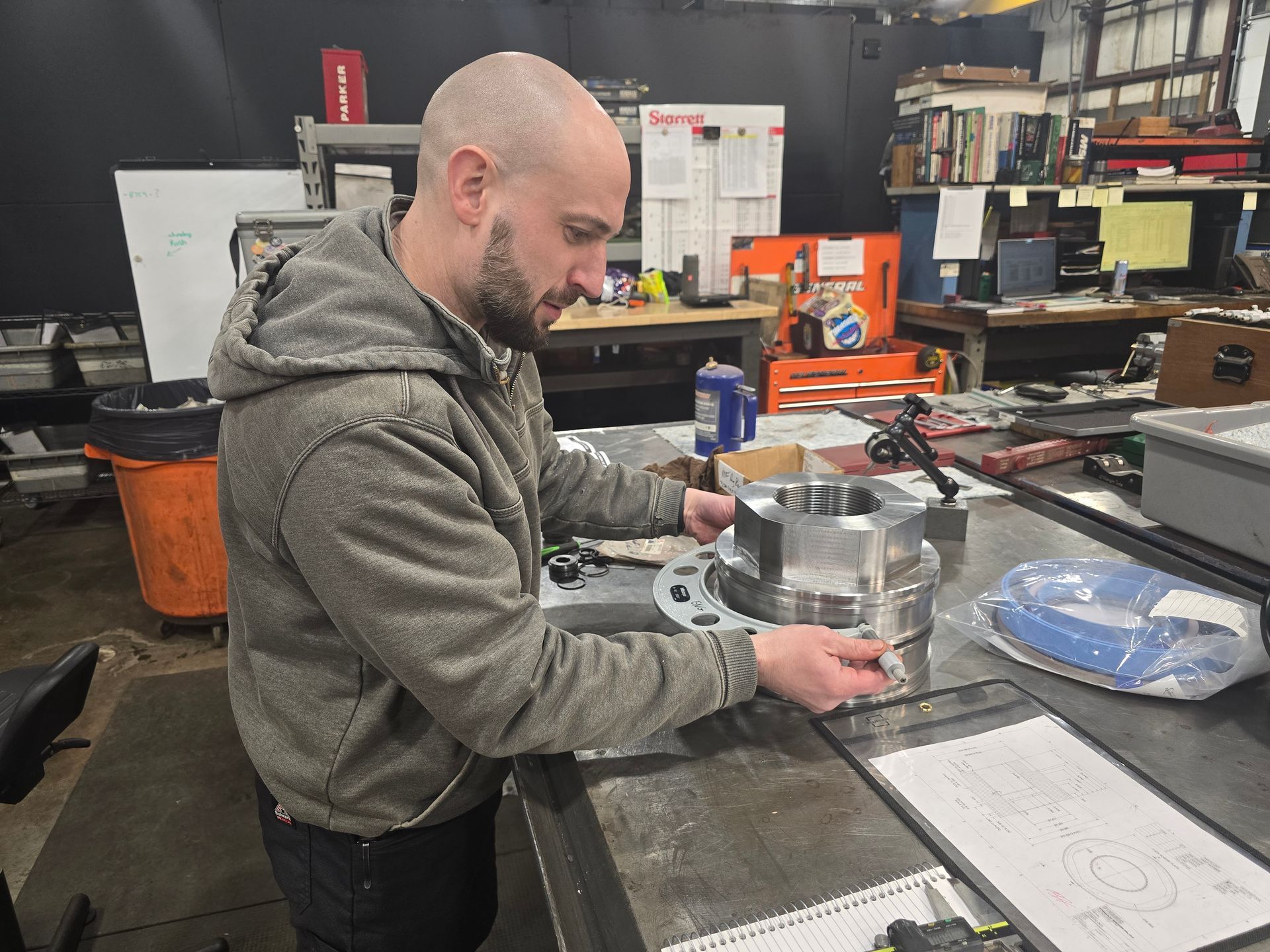 Man in a workshop inspecting a metal engine part on a workbench