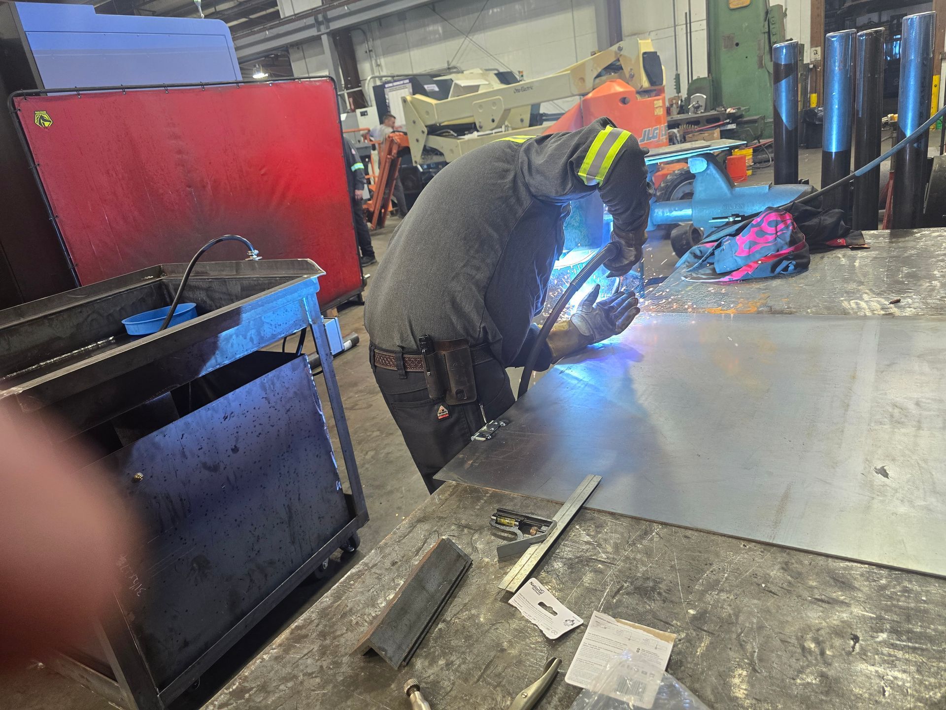 Worker welding metal in a workshop, sparks flying beside tools and equipment.