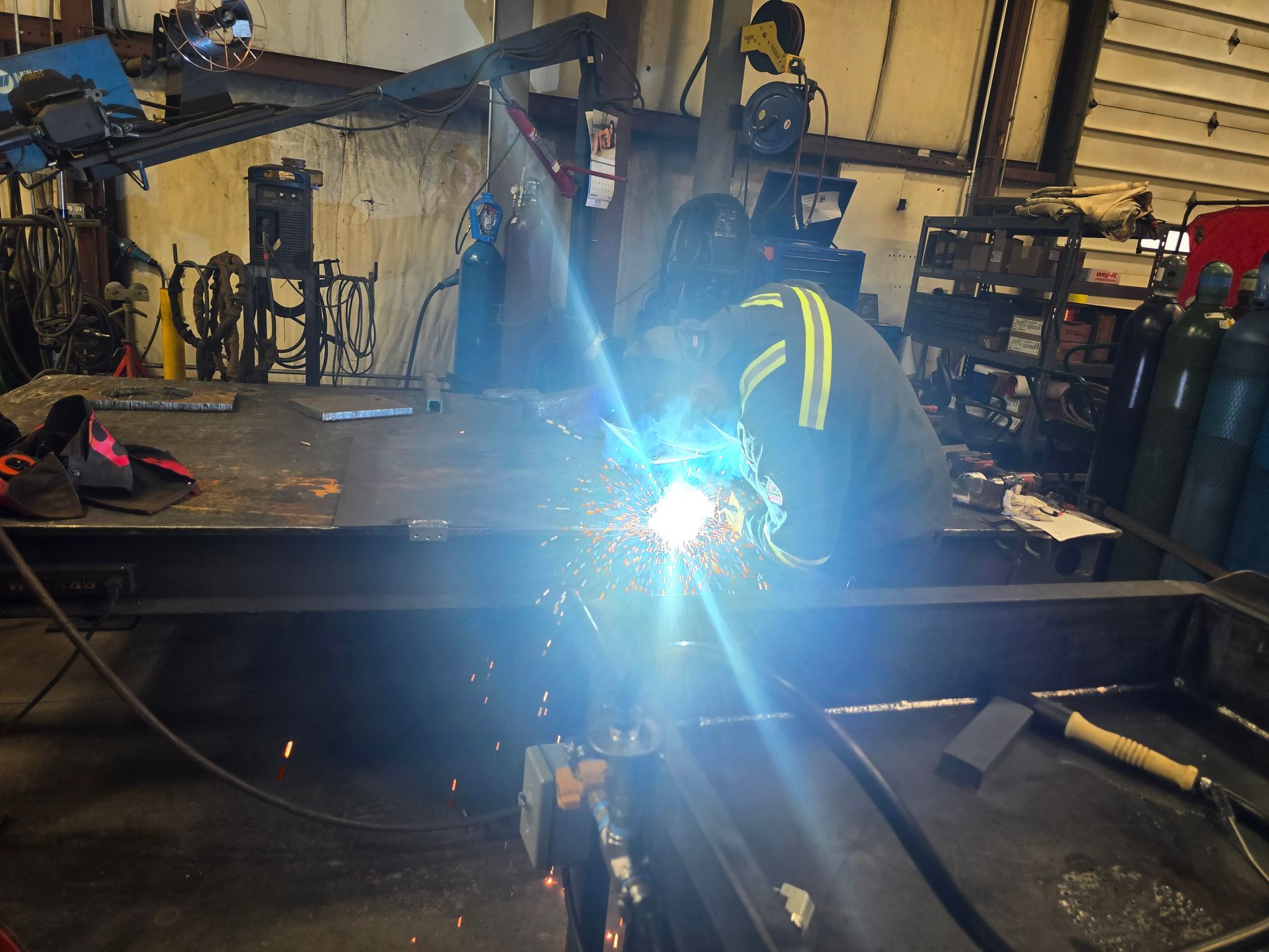 Worker welding metal in a dim workshop, bright blue arc light illuminating the scene.