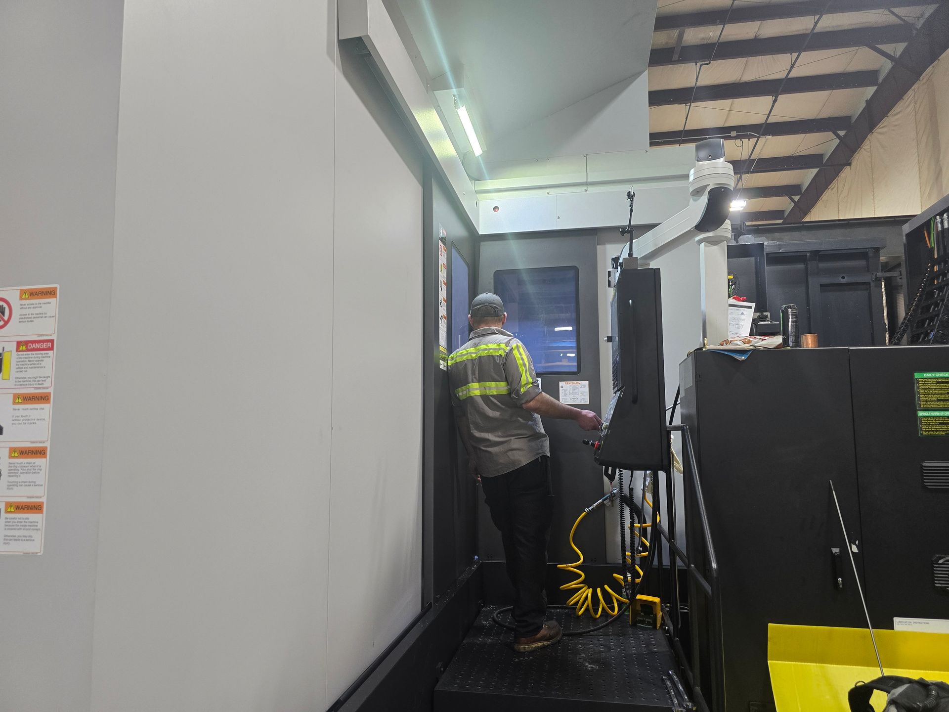 Worker in high-visibility jacket standing beside machinery in an industrial workshop corridor