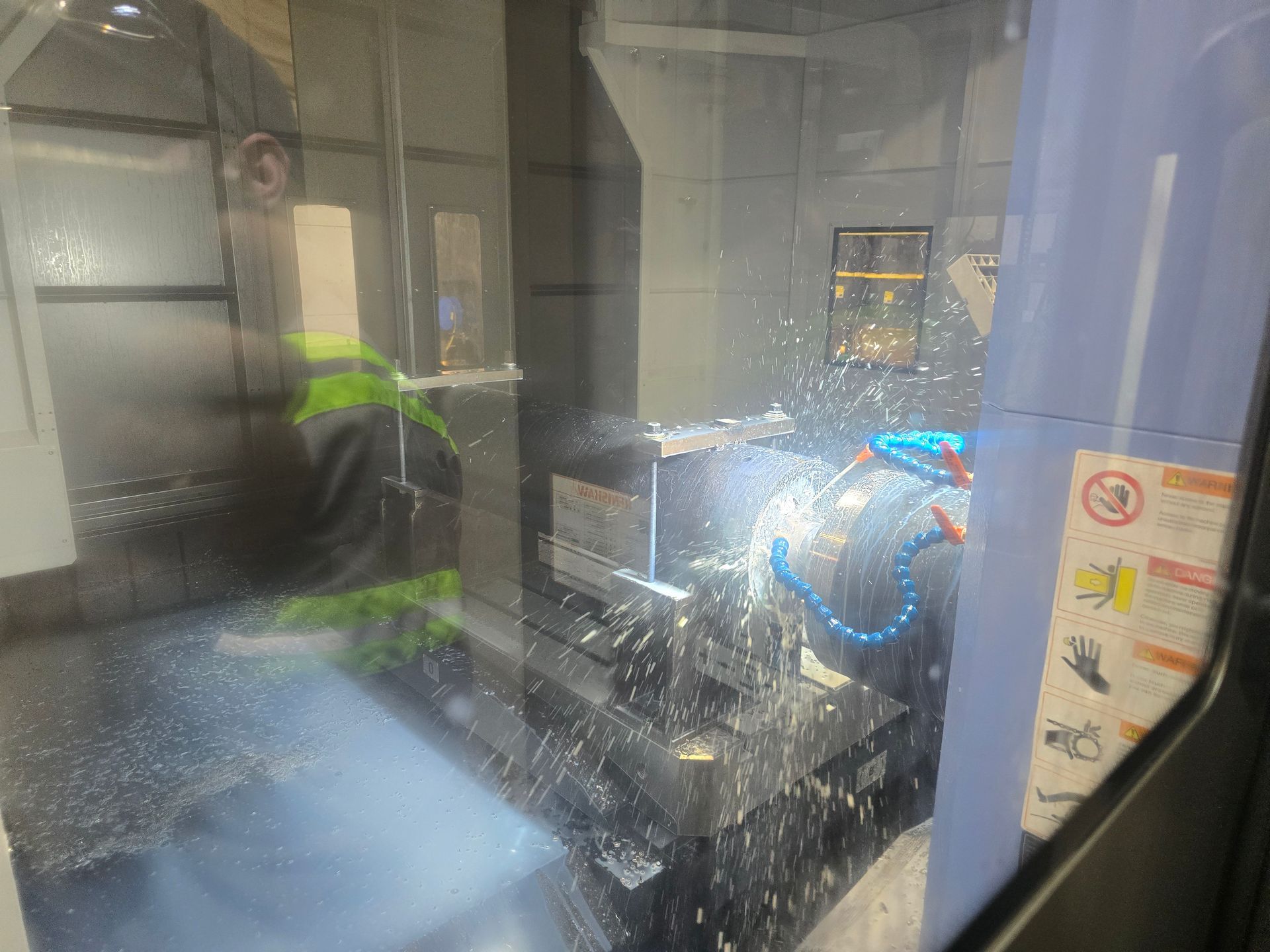 Industrial machine inside a glass enclosure, with bright blue and green lights reflecting on the panels.