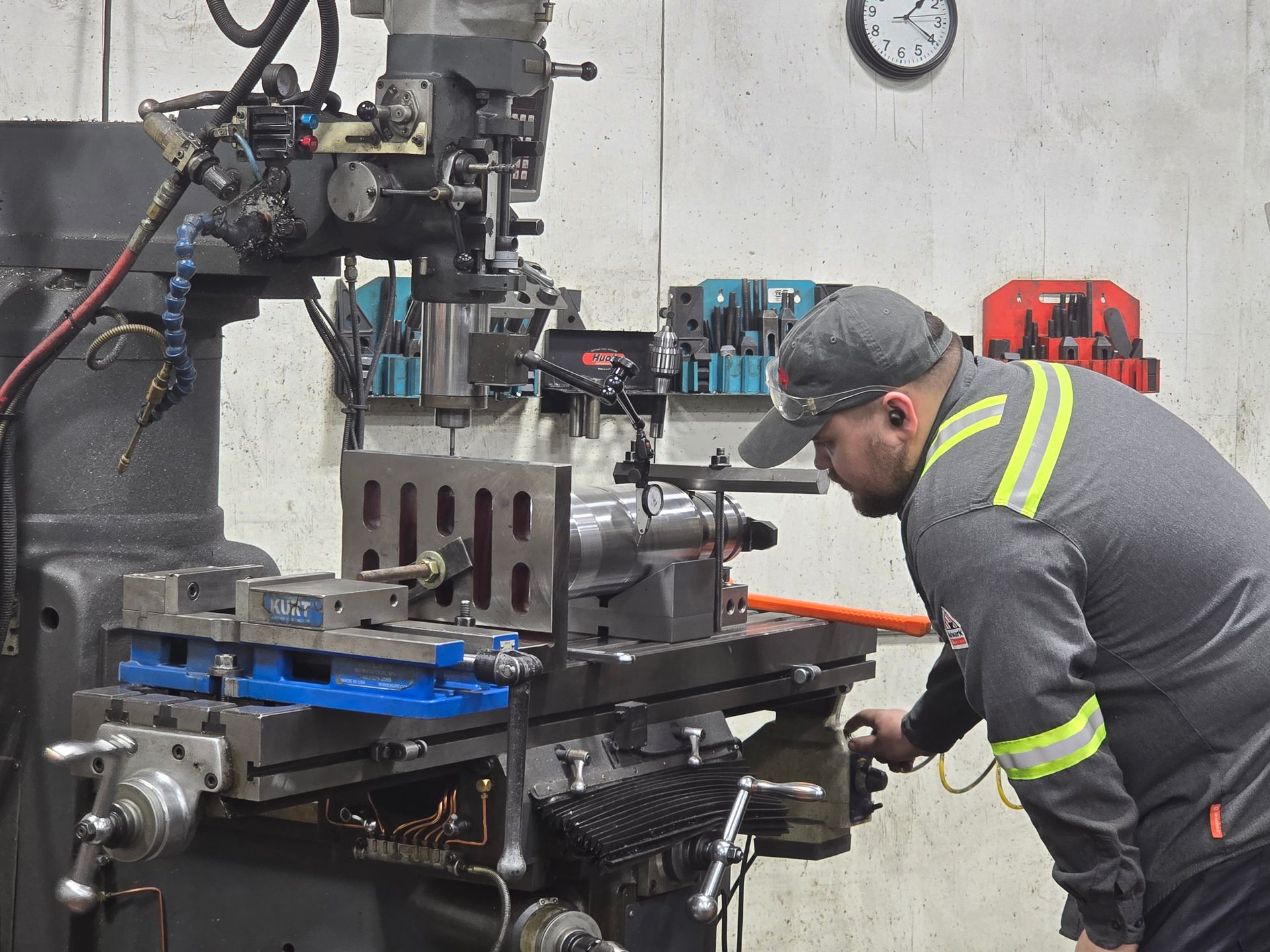 Worker operating a lathe in a machine shop, leaning toward the spinning metal workpiece.