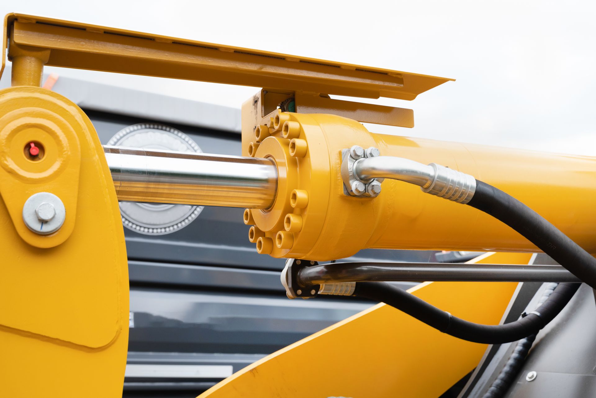 Yellow hydraulic cylinder with chrome rod and black hoses on heavy equipment.