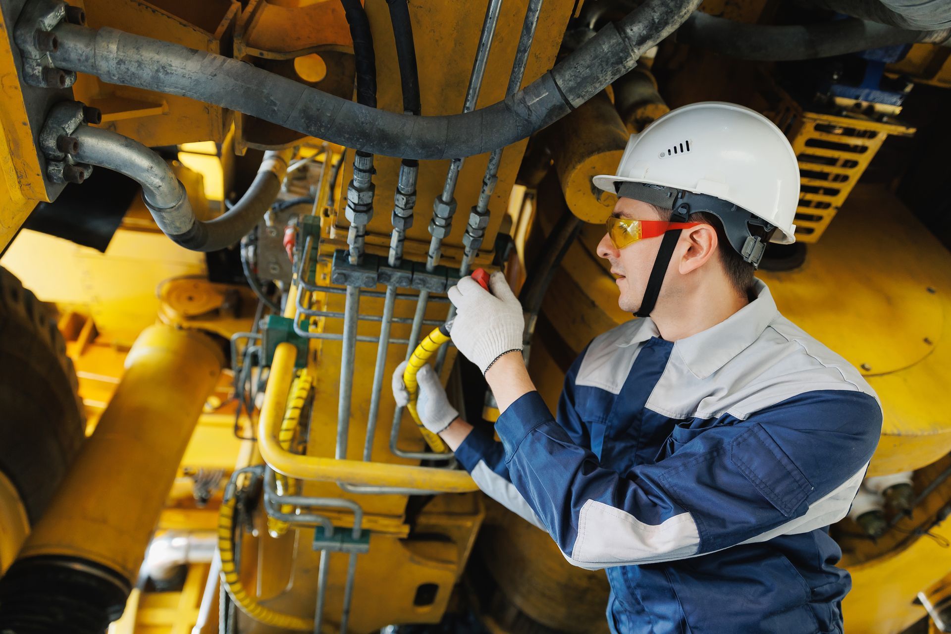 A male worker mechanic inspecting a hydraulic hose of a mining truck in a garage A male worker mechanic inspecting a hydraulic hose of a mining truck in a garage