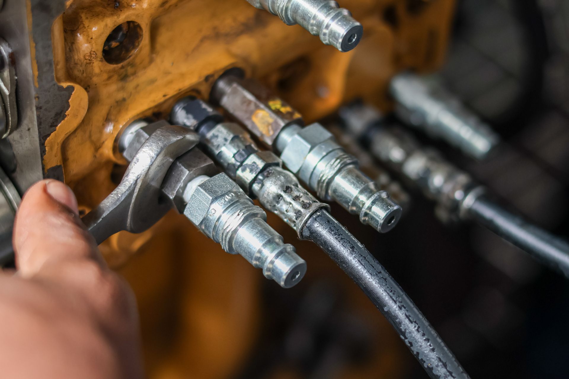 Technician tightening steel hydraulic quick-connect fittings with a wrench.
