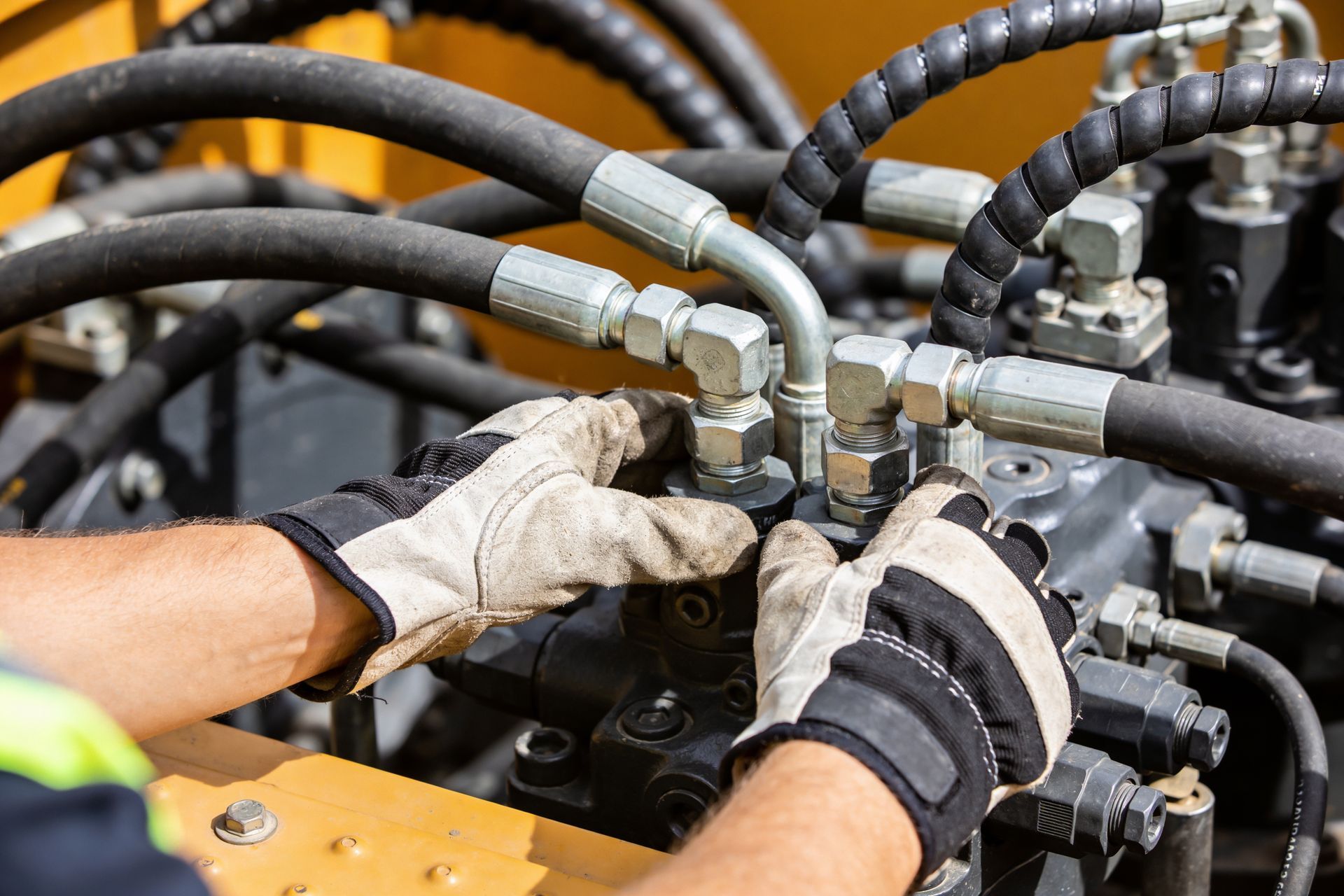 Technician tightening hydraulic hose fittings on industrial equipment.