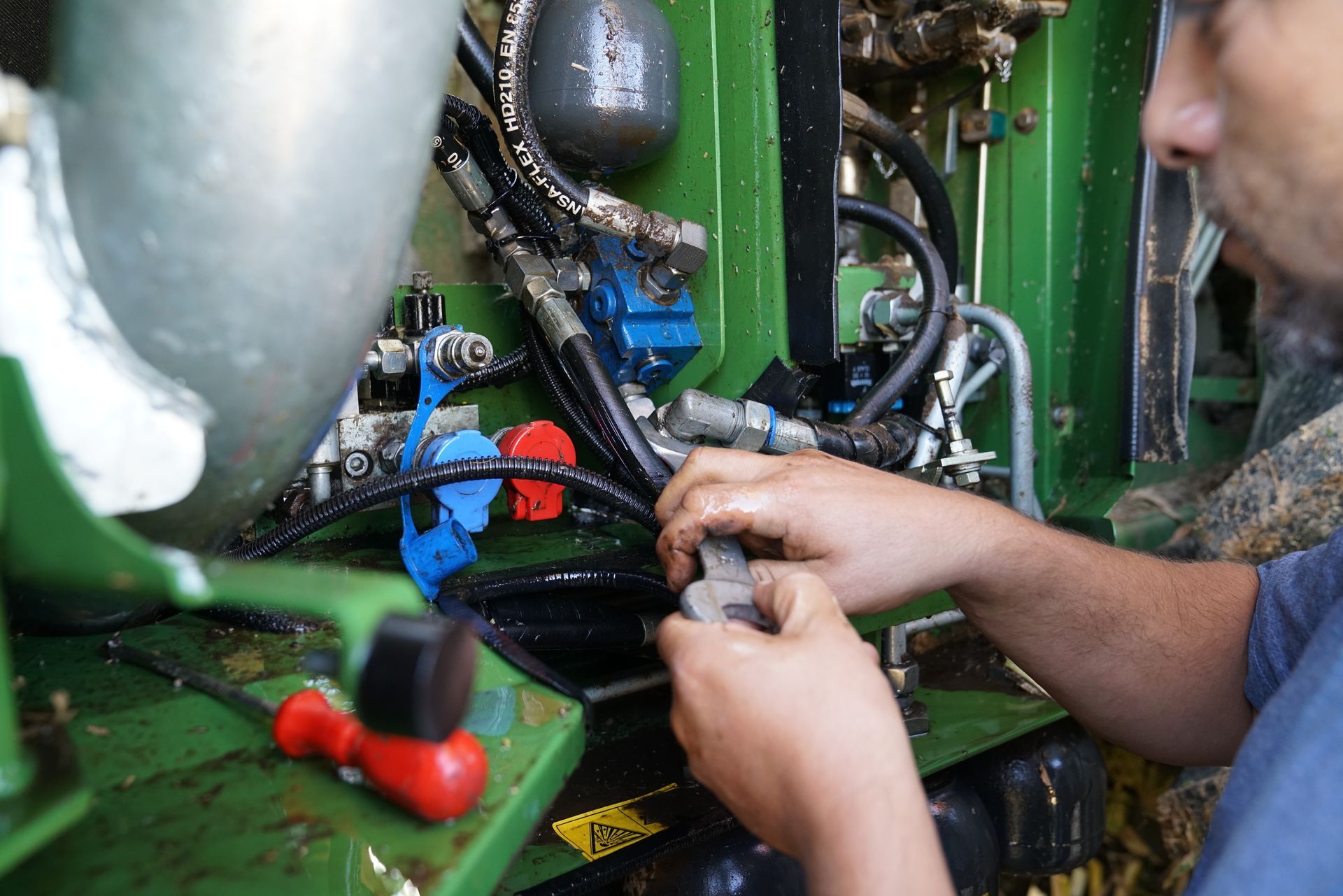 Technician tightening hydraulic fittings and hose connections on heavy equipment during a repair job