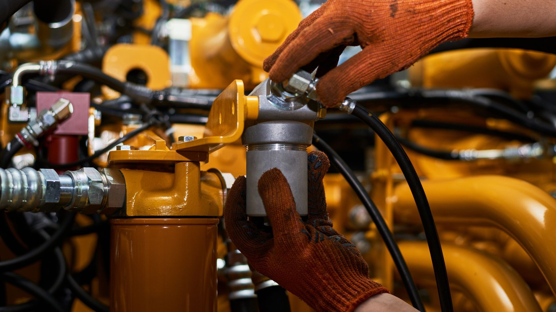 Hands in orange gloves working on a yellow engine component.