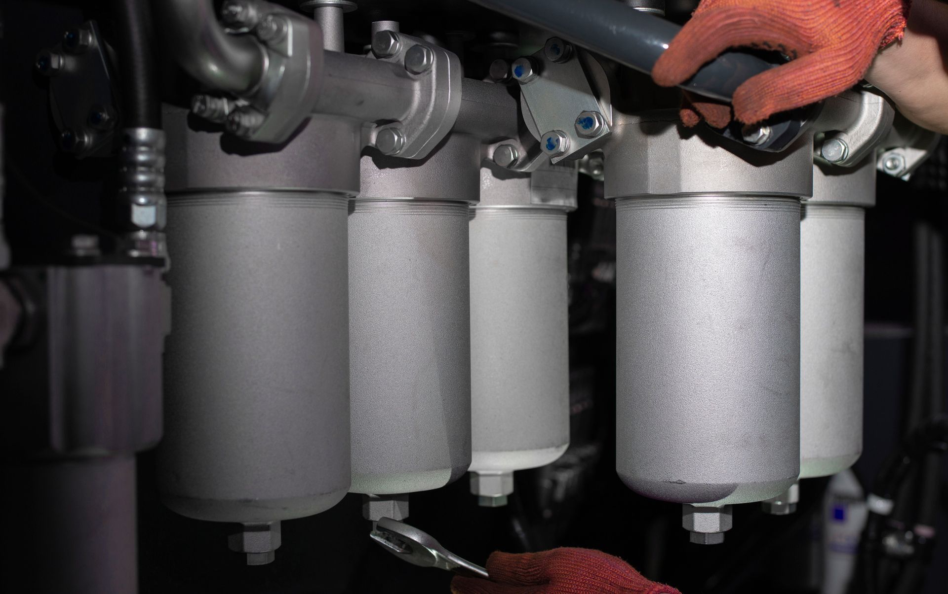 Person in red gloves working on industrial filters; metallic, mounted equipment.