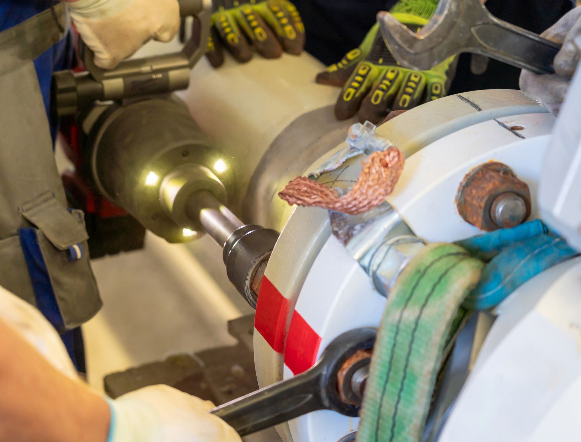 Workers using tools to repair machinery. Gloves, wrenches, and an impact wrench are visible.