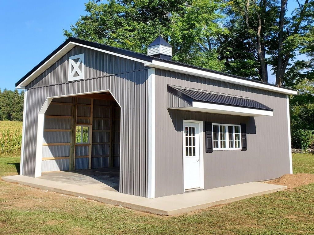 A gray barn with a white door and windows is sitting in the middle of a grassy field.