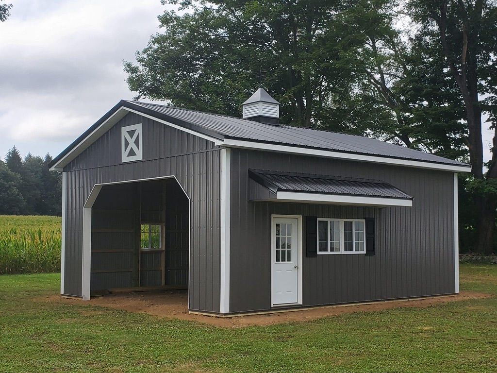 A gray barn with a white door is sitting in the middle of a grassy field.
