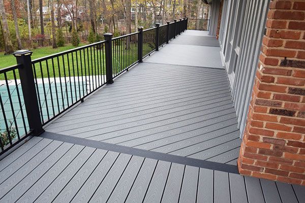 A gray deck with a black railing and a brick wall.