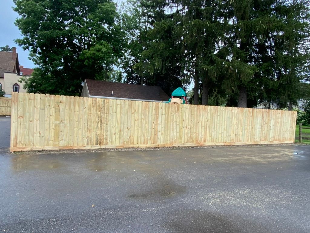 A wooden fence surrounds a parking lot with trees in the background