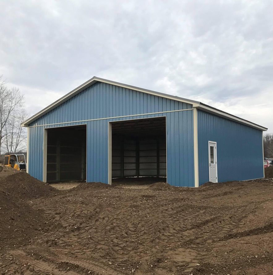 A blue metal building is sitting in the middle of a dirt field.