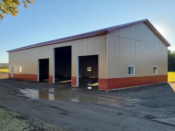 A large metal building with three doors is sitting on the side of a dirt road.