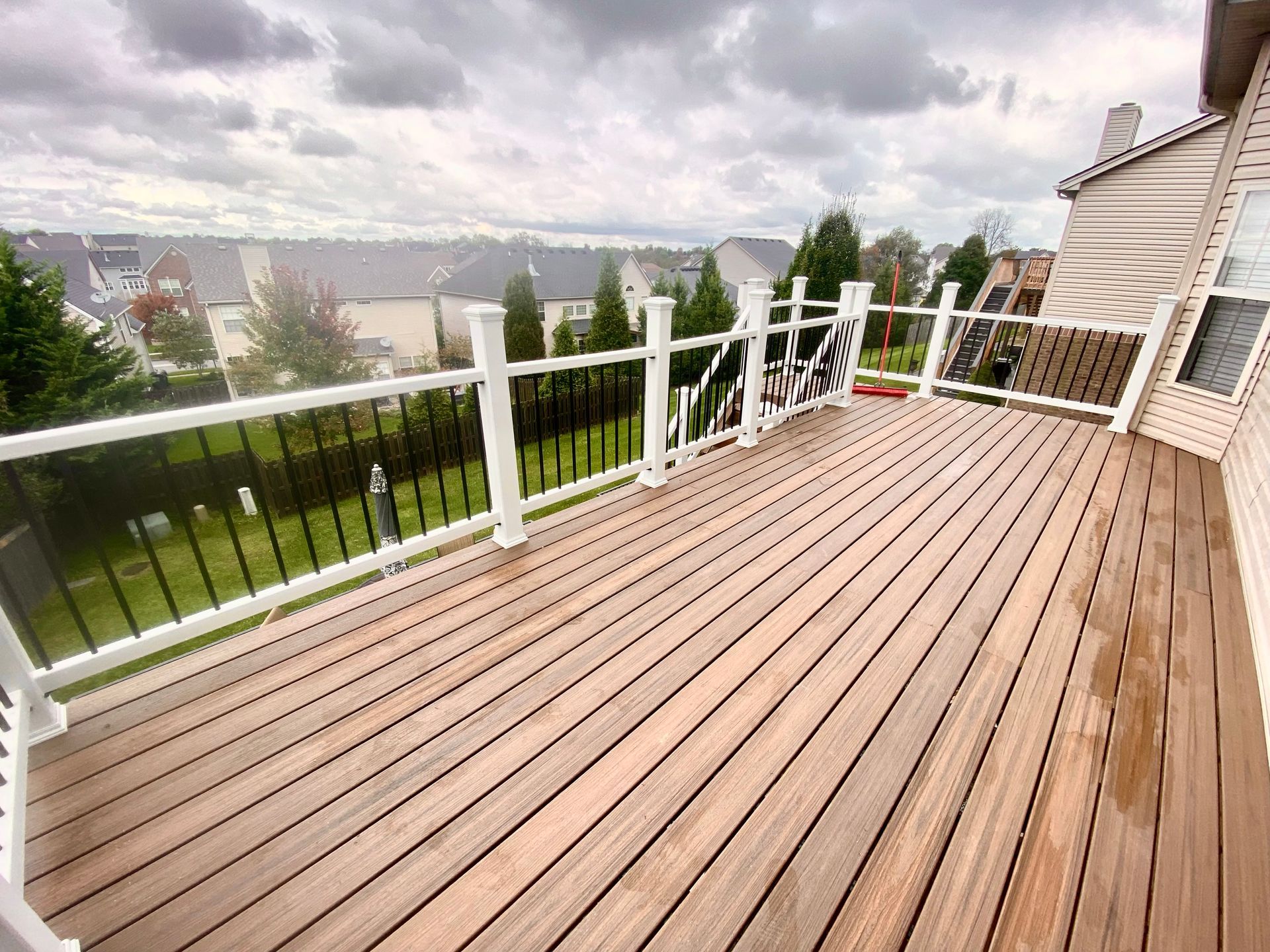 A large wooden deck with a white railing and a view of a lush green field.