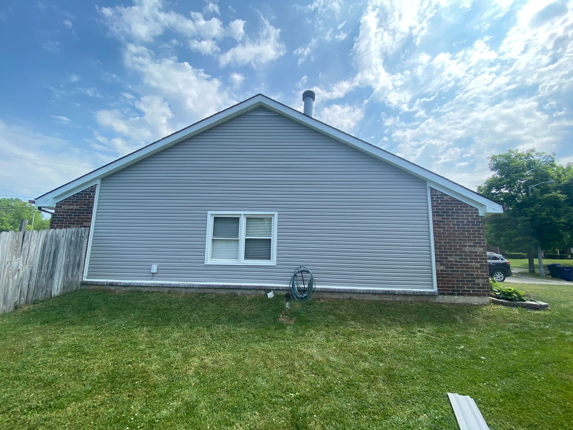 The back of a house with a white siding and a brick wall.