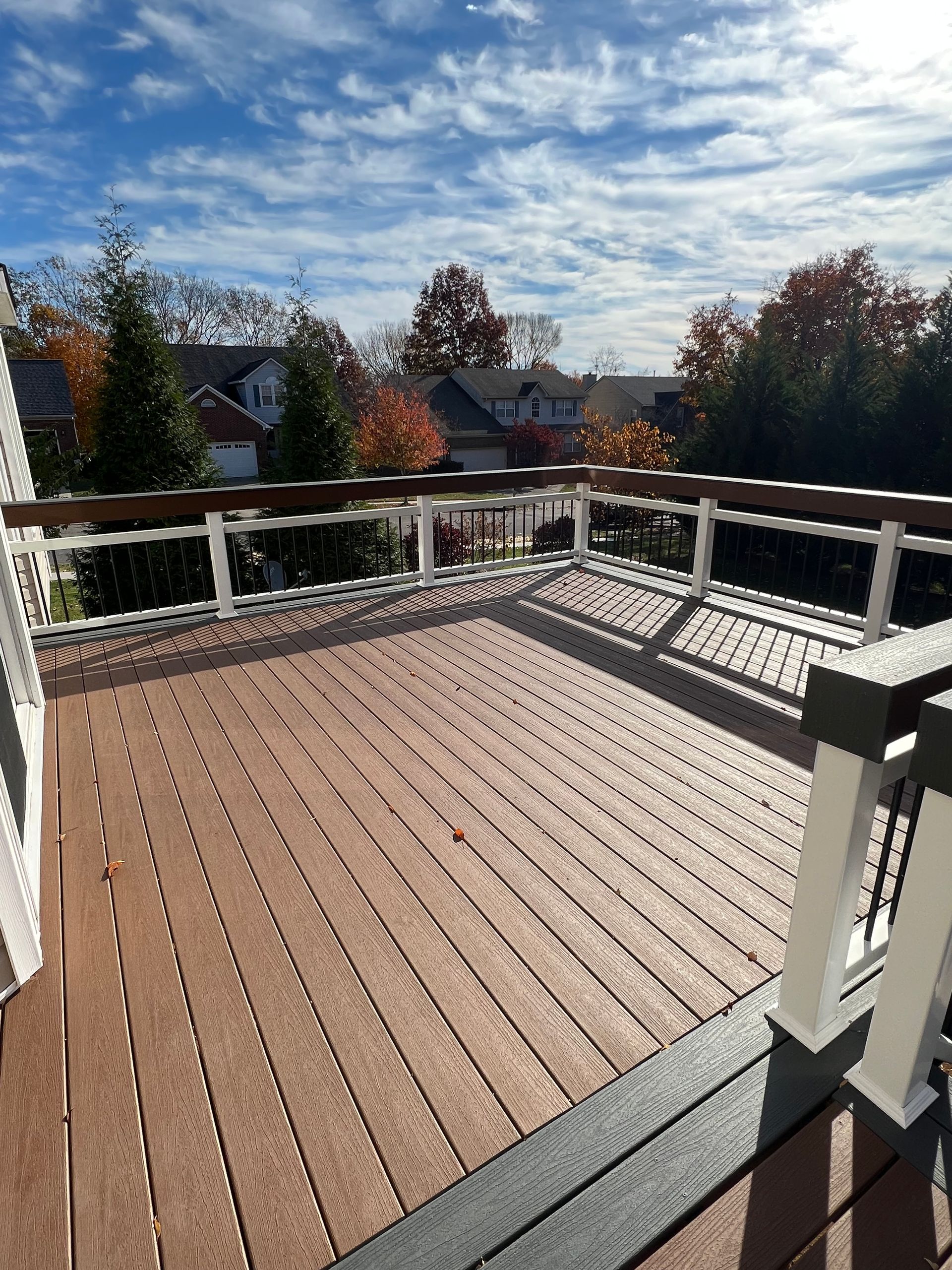 A large wooden deck with a white railing and a view of a city.