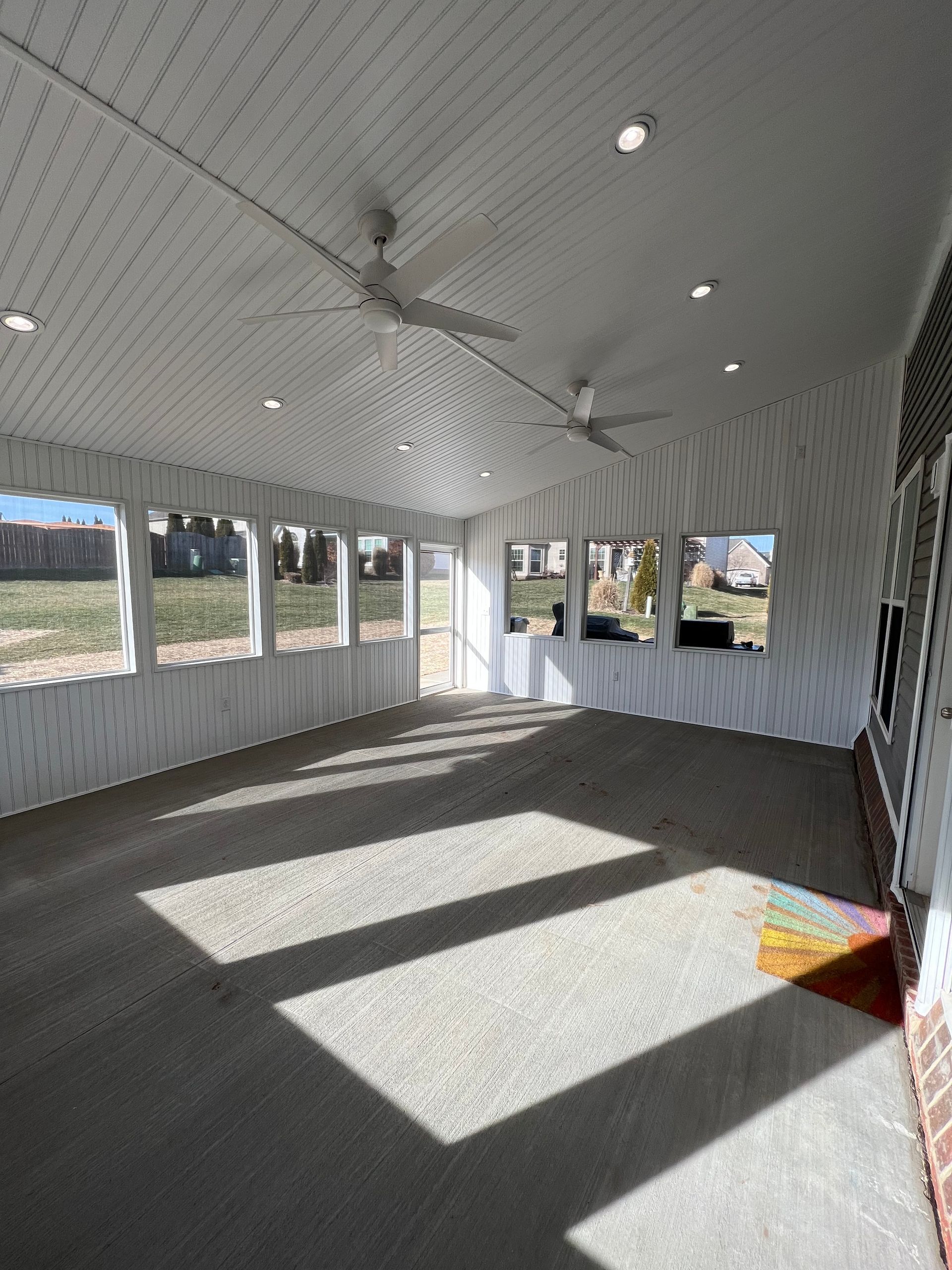 A screened in porch with a lot of windows and a ceiling fan.