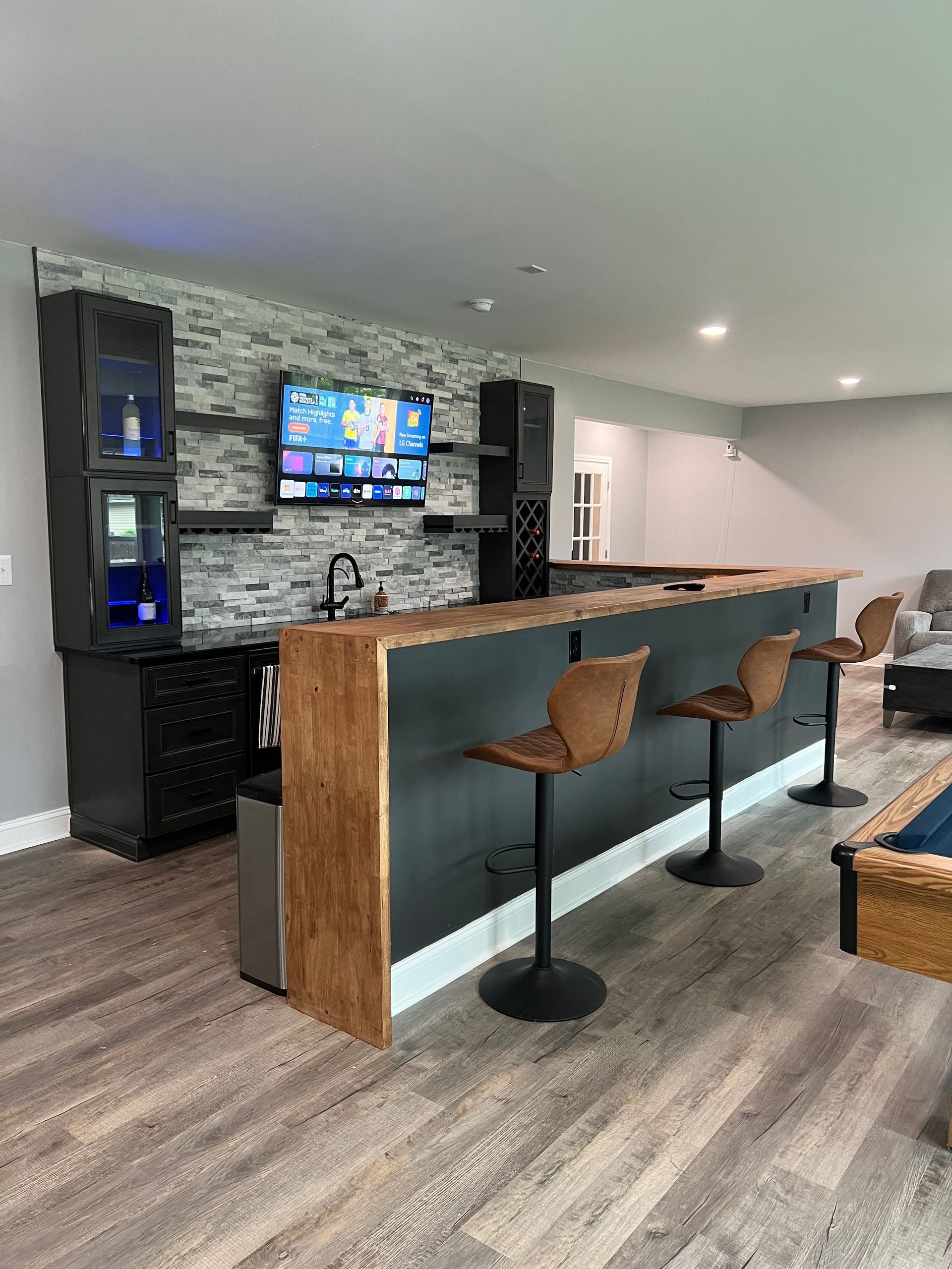 A living room with a bar , stools , a pool table and a television.