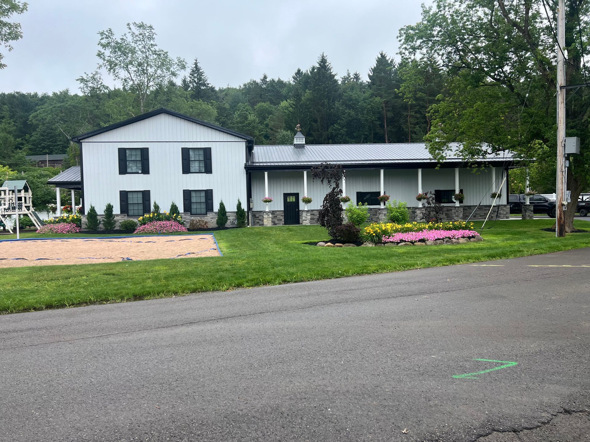 A large white house with black shutters is sitting on the side of a road.