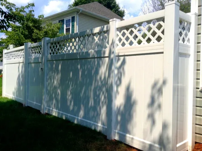A white fence with a lattice design is in front of a house.
