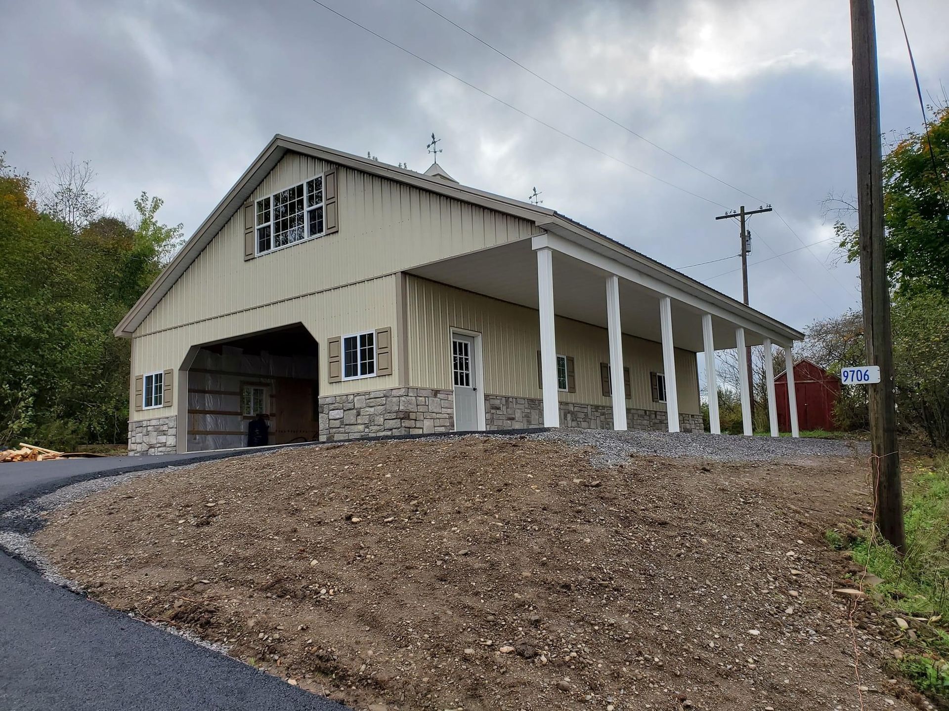 A large barn with a porch is sitting on top of a dirt hill.