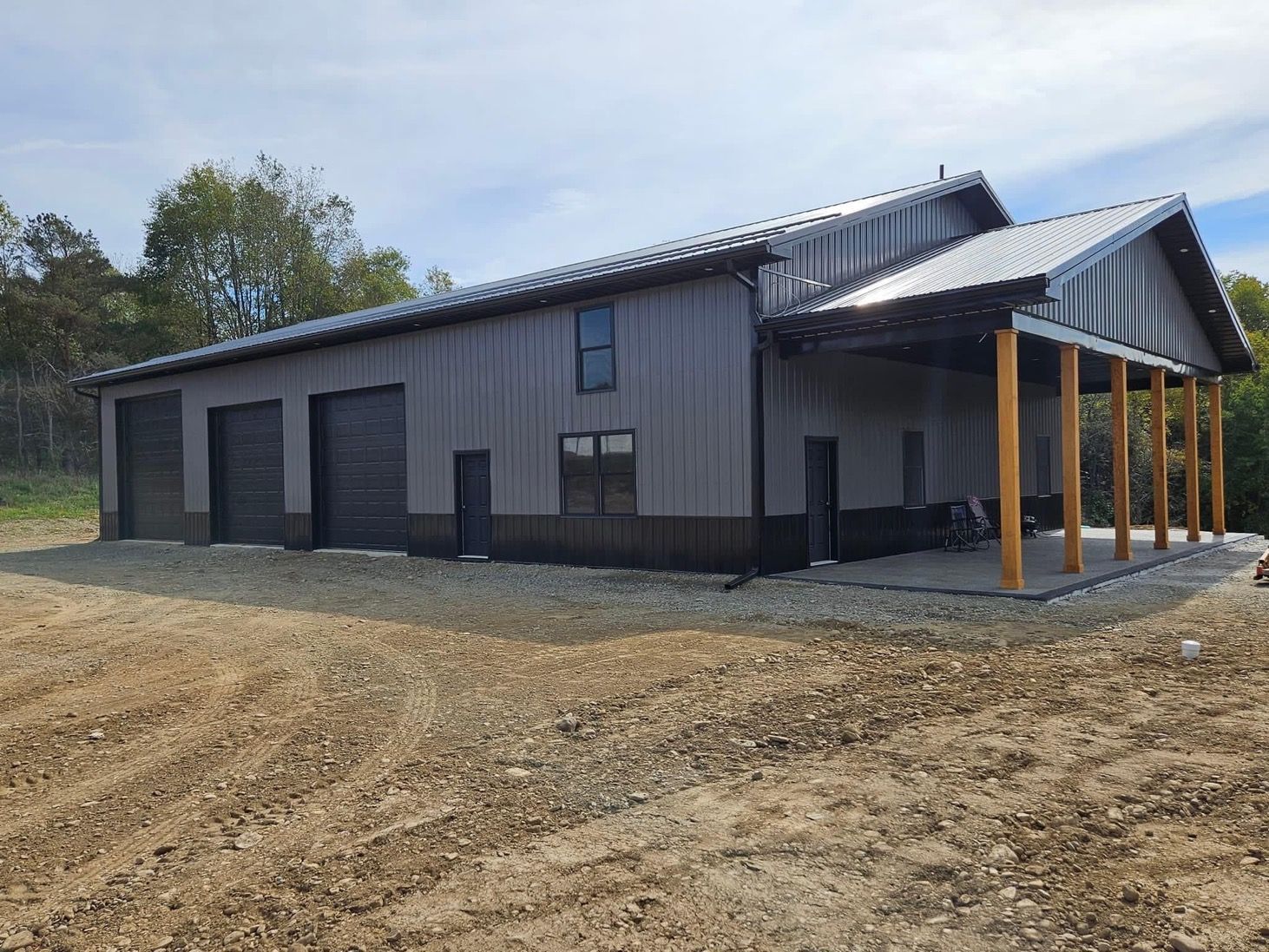 A large metal building with a porch and garage doors is sitting in the middle of a dirt field.