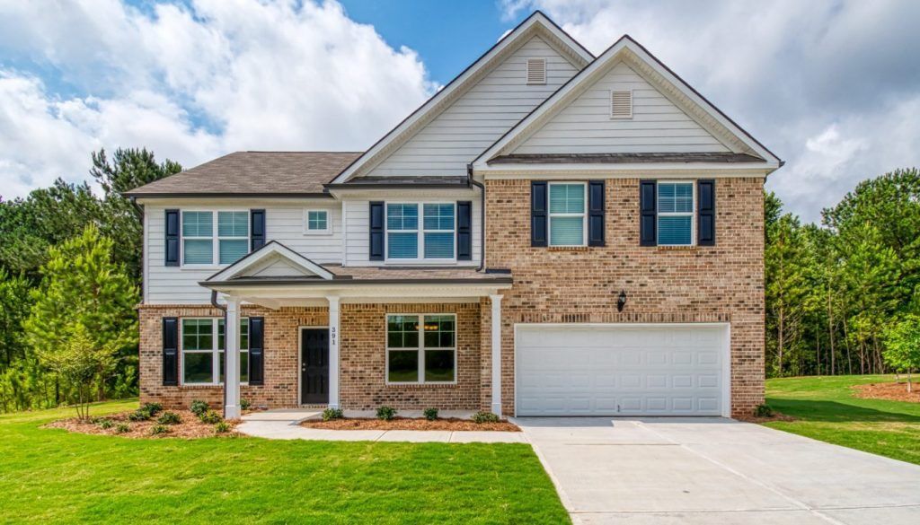 A large brick house with a white siding and black shutters is sitting on top of a lush green field.