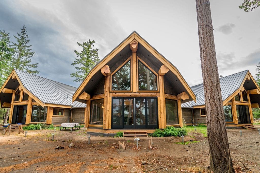 A large wooden house with a lot of windows is surrounded by trees.