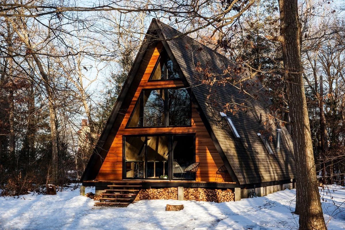 A small a frame cabin in the middle of a snowy forest.