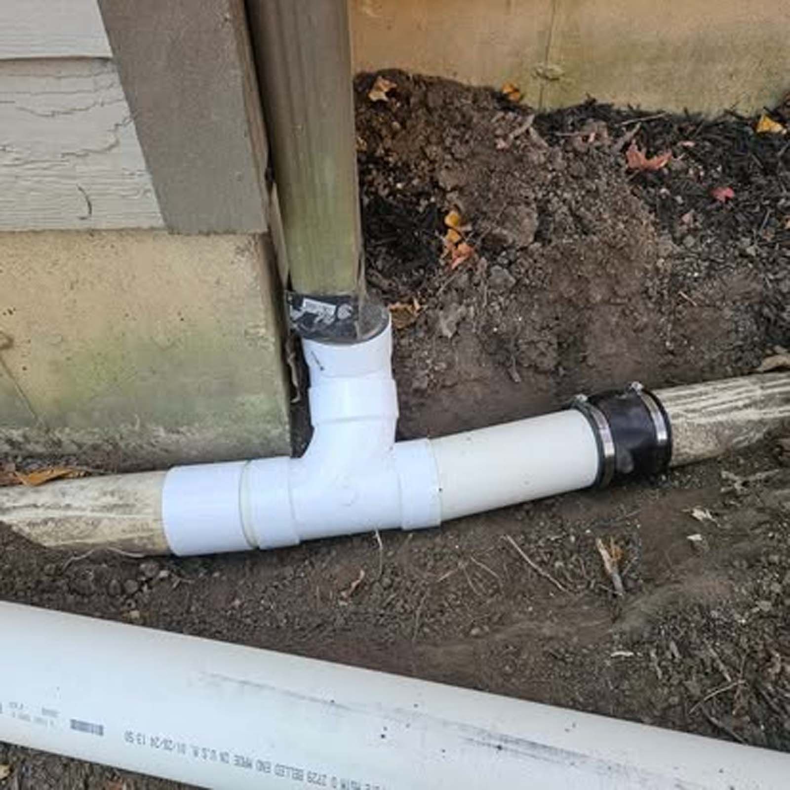 A white pipe is sitting in the dirt next to a wooden pole.
