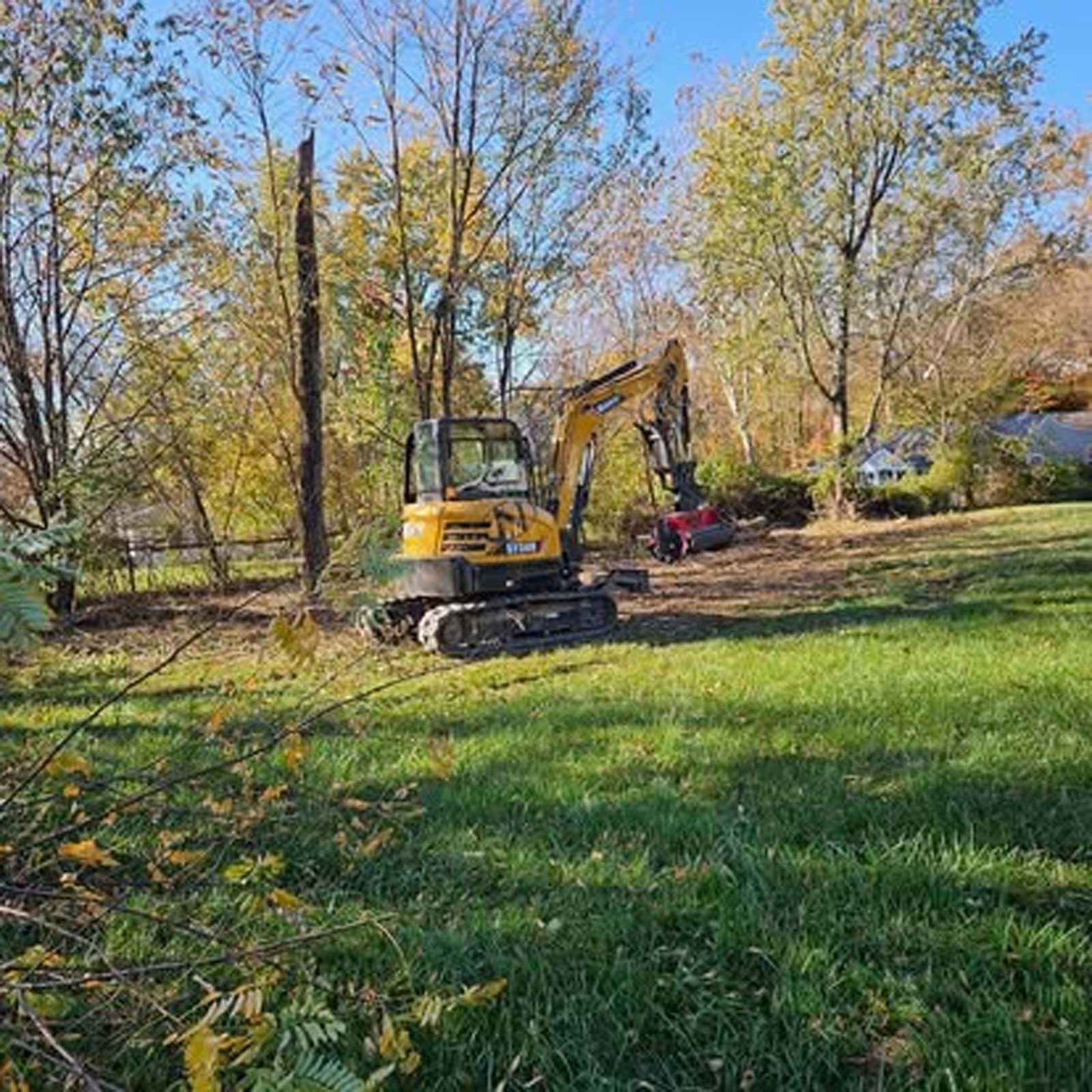 A yellow excavator is sitting in the middle of a grassy field.