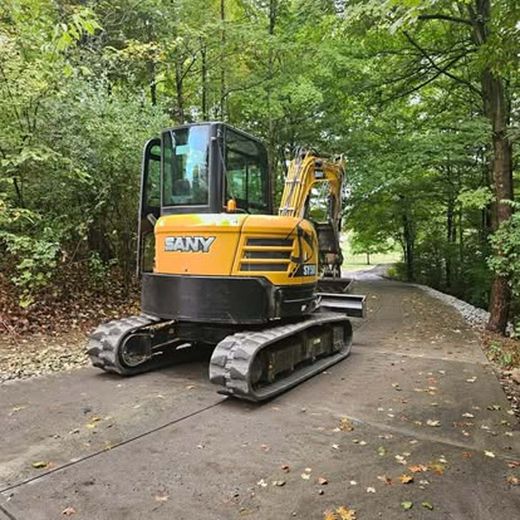 A yellow excavator is parked on the side of a road in the woods.