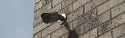 Wall-mounted security camera on a brick building, casting a shadow in sunlight