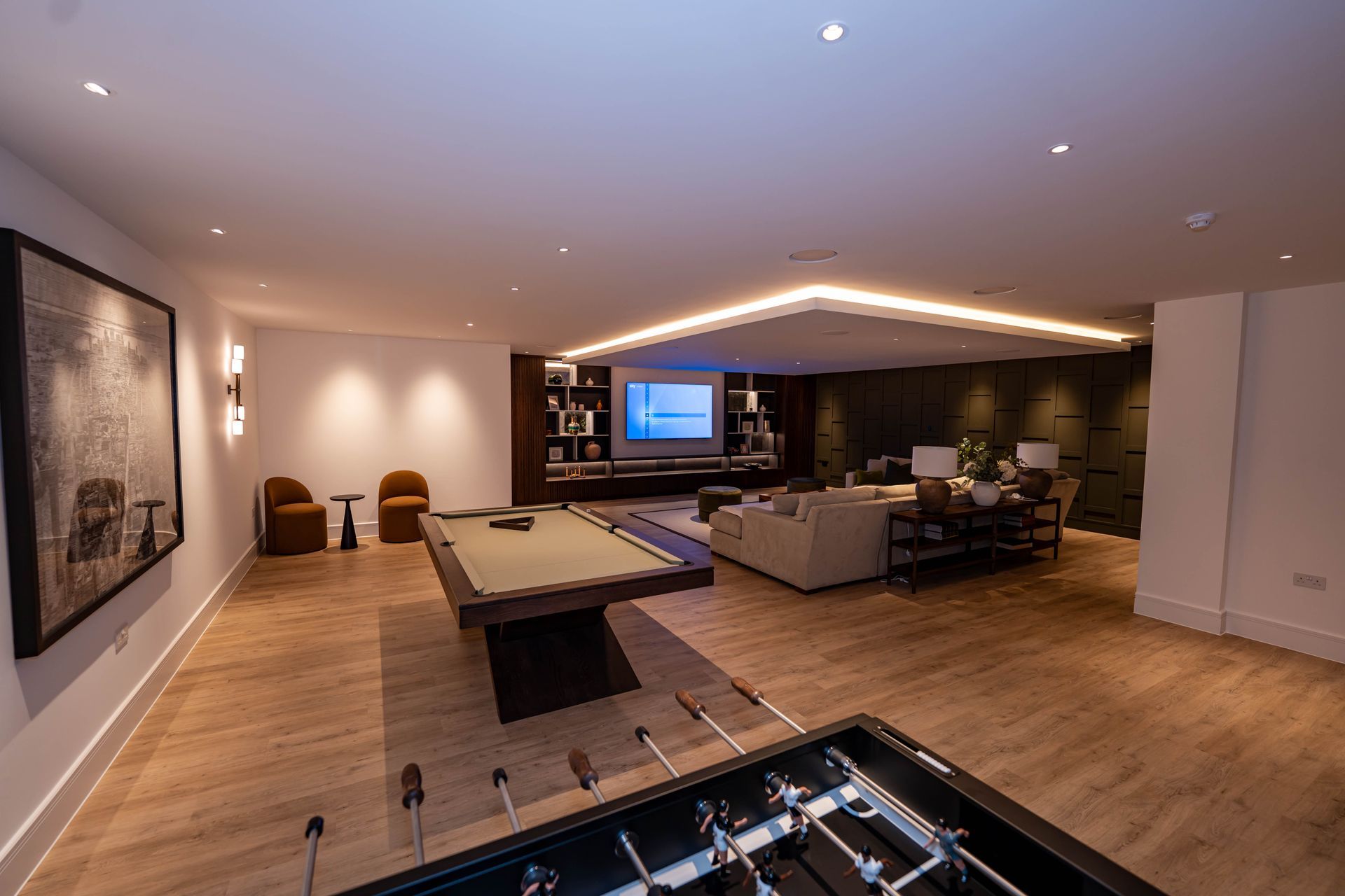 Modern open-concept living room with wood floors, sectional sofa, pool table, and TV in the background