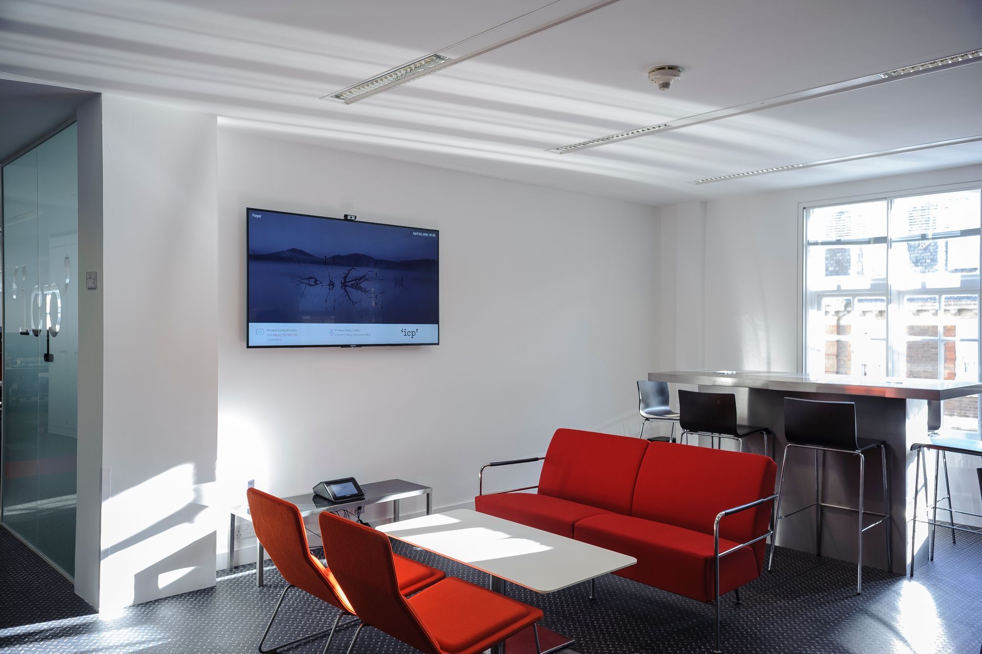 Modern living room with red sofa, orange chairs, wall TV, and large bright windows